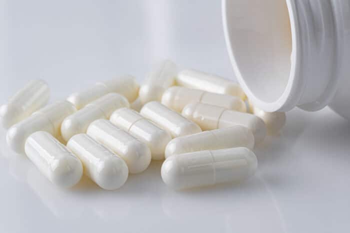 White plastic medicine vial can bottle with white capsules on white background.
