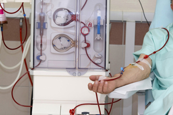 Patient sits by dialysis machine.