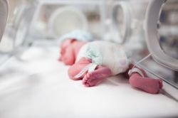 Newborn baby boy covered in vertix inside incubator