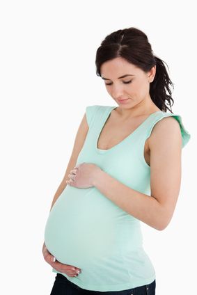 Young pregnant woman looking at her belly against white background