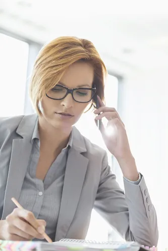 Young businesswoman on call while writing at desk in office