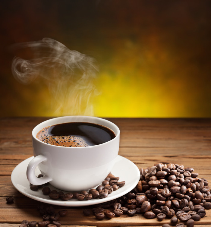 Cup of coffee with coffee beans near it on old wooden table.