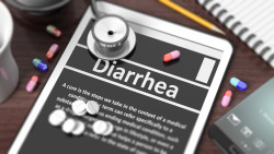 Tablet with "Diarrhea" on screen, stethoscope, pills and objects on wooden desktop.