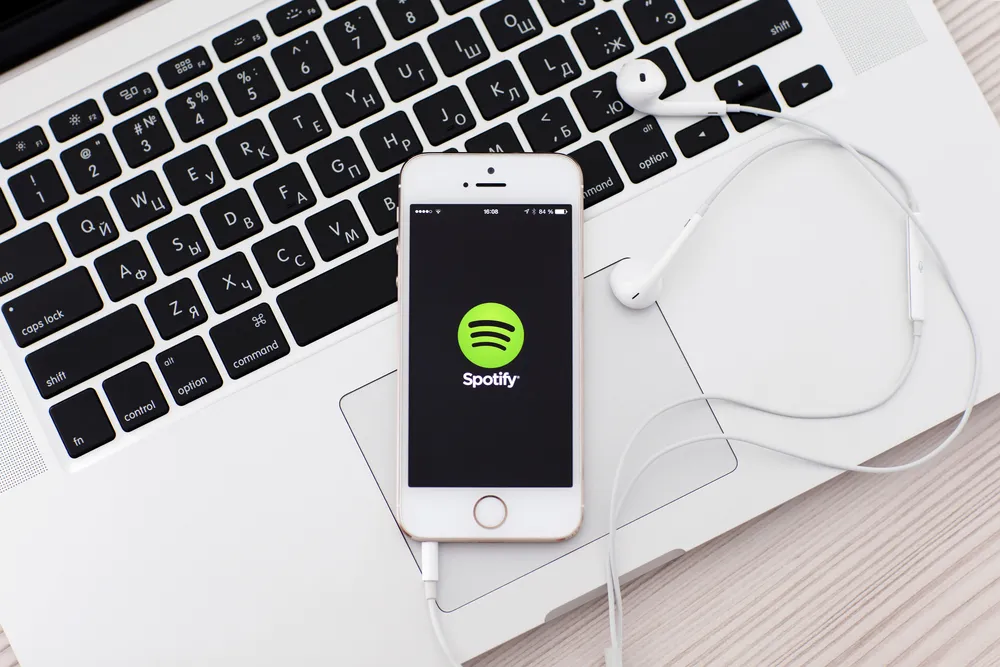 White iPhone 5s with site Spotify on the screen and headphones l