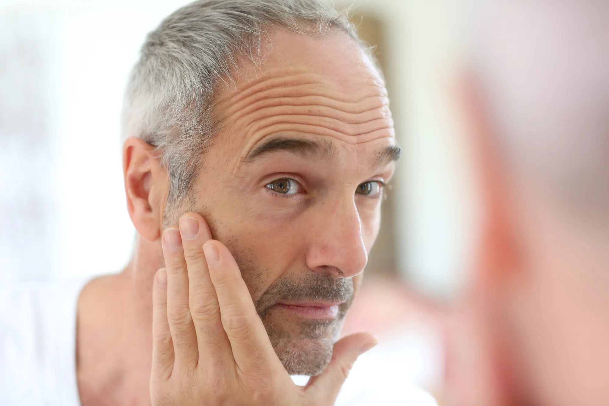Mature man in front of mirror applying cosmetics
