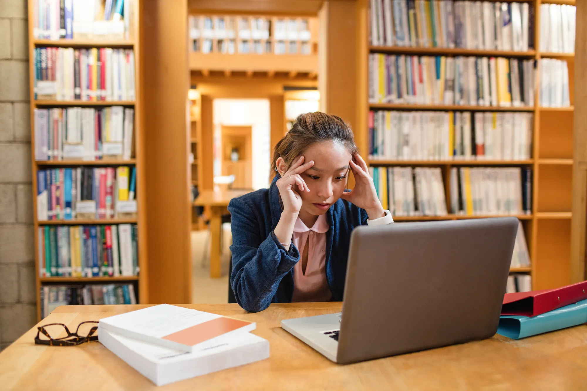 Tensed young woman using laptop in library at college