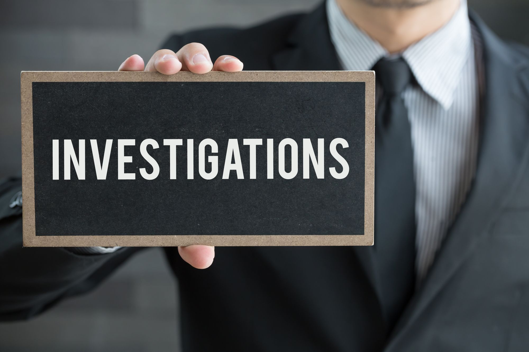 A man in suit holding out an "Investigations" sign in one hand — lawsuit investigations, class action investigation