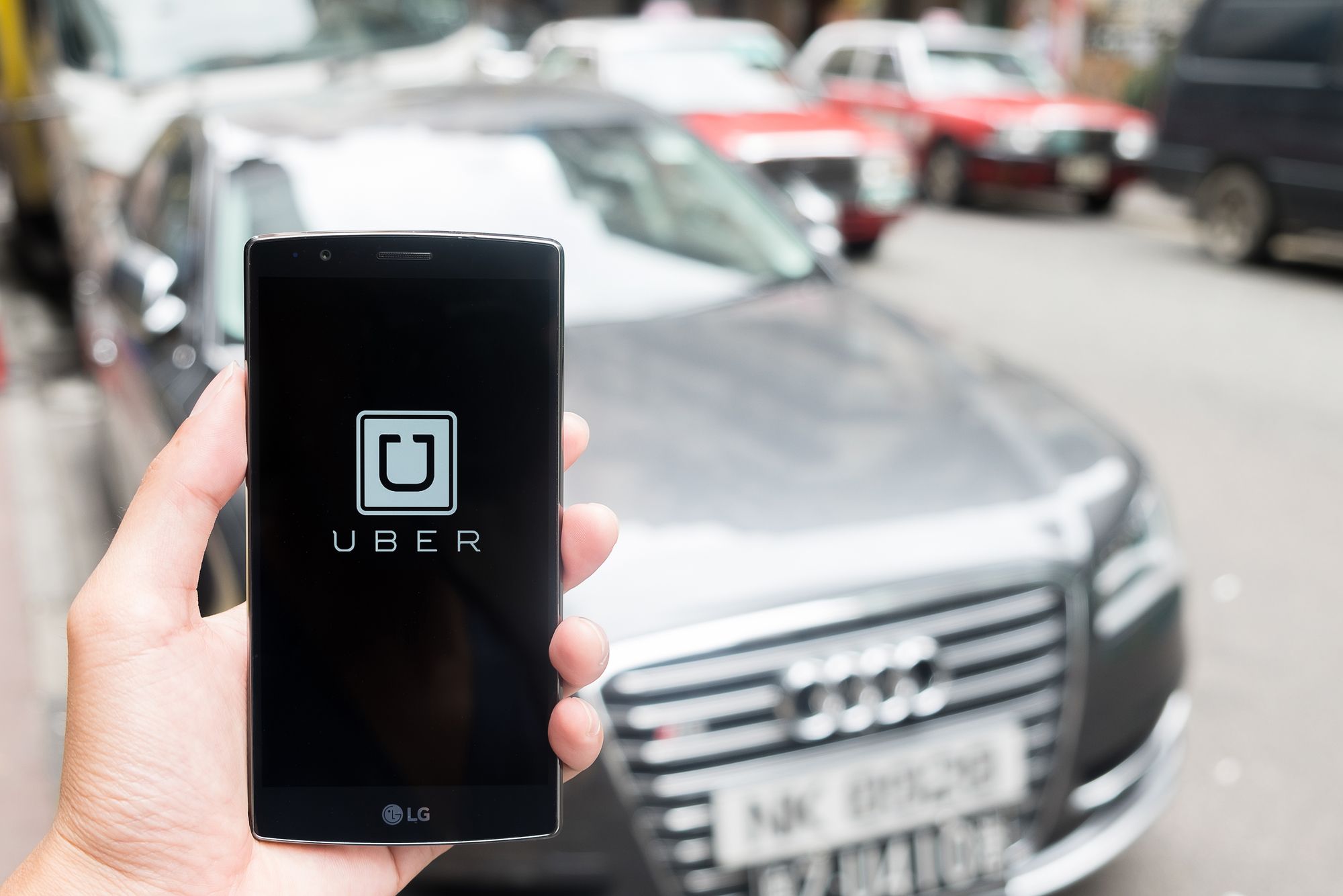 HONGKONG,CHINA - MAY 16,2016 : A man hand holding Uber app showing on LG G4 on road and red car, Uber is smartphone app-based transportation network.