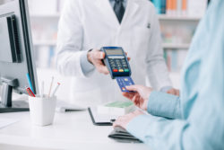 Woman at the pharmacy purchasing medicines and medical products, she is inserting the credit card in the terminal
