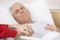 Senior man in hospital bed holding wife's hand