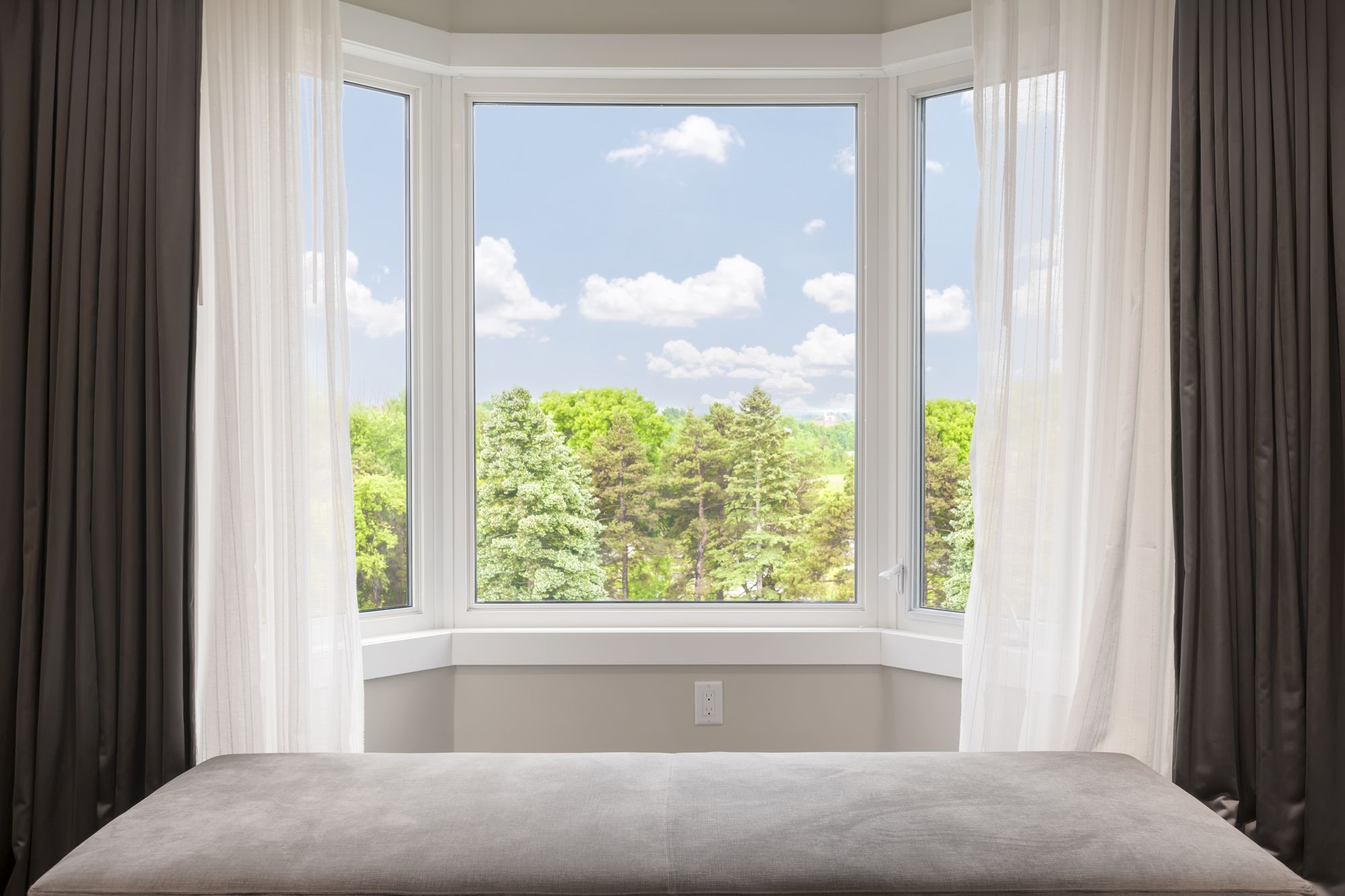 Bay window with drapes, curtains and view of trees under summer sky