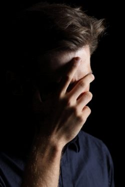 Worried or embarrassed man covering his face with hand isolated on a black background