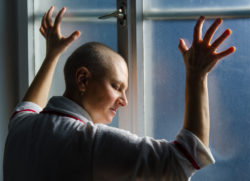 Bald woman suffering from cancer leaning on the hospital window.