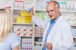 Mature male pharmacist taking out prescribed medicine for customer in pharmacy