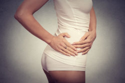 Young female touching her right side in pain. Kidney inflammation and therapy. Medicine and health care concept. Gray background