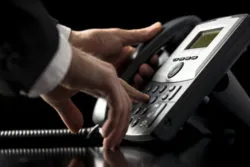 Low angle closeup view of the hands of a businessman in a suit dialing out on a telephone call using a dial-up desktop landline instrument as he presses the numbers on the keypad