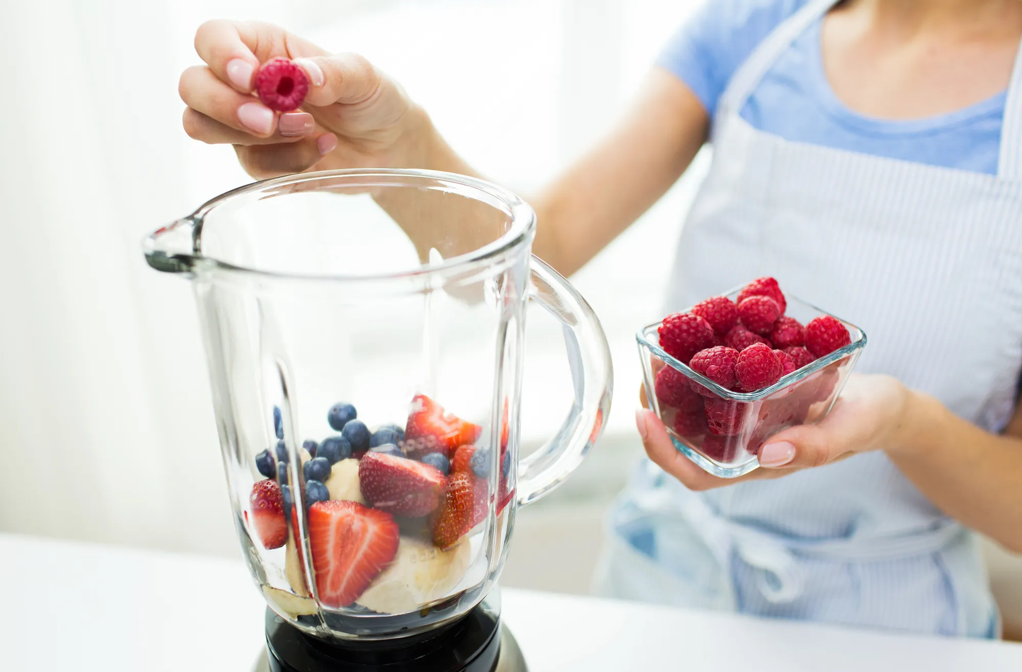 healthy eating, cooking, vegetarian food, diet and people concept - close up of woman with blender making fruit shake at home