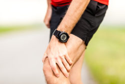 Runner holding sore leg, knee pain from running or exercising, jogging injury or cramp, cross country in summer nature