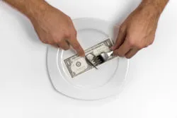 Single one dollar bill on the middle of a plate, knife and fork.