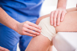 Doctor is rewinding knee bandage to young woman.