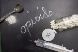 Opioids written in chalk on blackboard with crushed powder, spoon, syring and prescription vial.