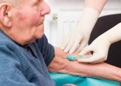 Doctor taking blood sample from elderly patient to monitor anticoagulant treatment.