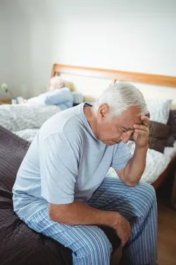 Frustrated senior man sitting on bed in bedroom