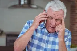 Worried senior man talking on mobile phone at home