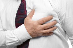 Elderly man holding hand on chest suffering from heart attack, closeup