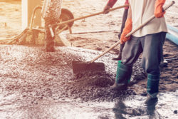 man workers spreading freshly poured concrete mix on building with vintage tone.