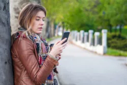 Closeup portrait upset skeptical unhappy serious woman talking texting on phone displeased with conversation isolated park trees outdoors background. Negative human emotion face expression feeling
