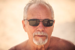 portrait of grey haired bearded old man in modern black sunglasses against light background