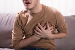 Close-up Of A Young Man Sitting On Sofa Having Heart Attack At Home