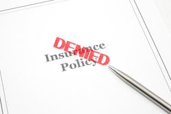 An insurance policy and a pen and the word Denied in red stamp across the policy.