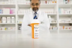 Bottle of pills on desk with a mature male pharmacist in the background