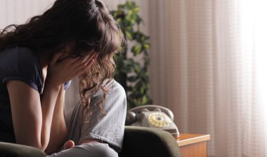 Depressed young woman sitting in chair at home