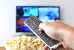 Remote control in the hand against pop-corn and TV-set