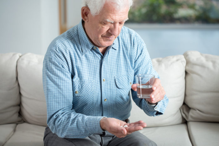 Ill senior man taking pill and drinking water