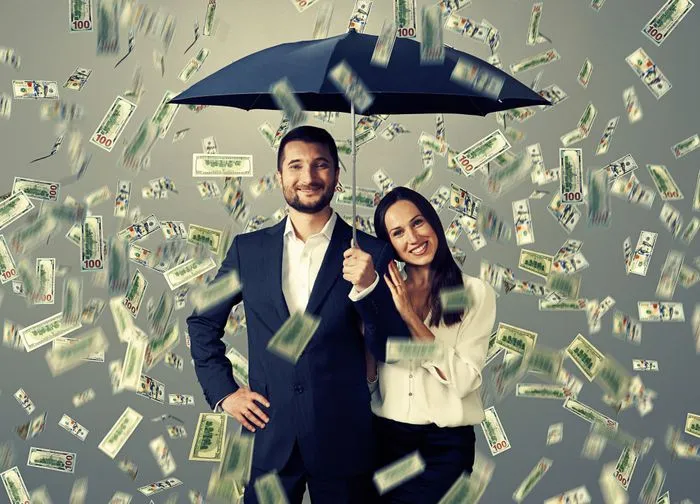 smiley successful couple with umbrella standing under money rain