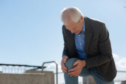 Our body can tell us a lot. Dismal frustrated old man raising himself onto his knee holding hands on it while feeling terrible pain