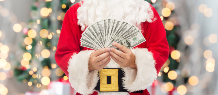 santa holding cash in front of a christmas tree