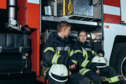 Two firefighters sit by a fire truck.