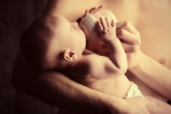 Infant drinking formula in the arms of a male