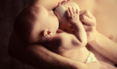 Infant drinking formula in the arms of a male