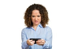 A woman looks annoyed while reading from her smartphone.