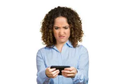 A woman looks annoyed while reading from her smartphone.