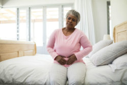 A woman sitting on a bed with stomach pain.