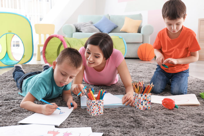 au pair laying on the floor encouraging to young kids to draw and color