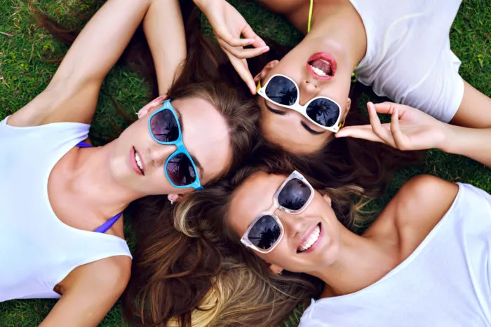 three young women laying on grass wearing Blenders eyeware sunglasses