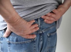 male hand holding hip in pain, blue jeans